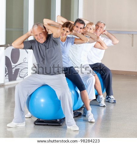 Happy senior citizens doing back exercises on gym ball in fitness center