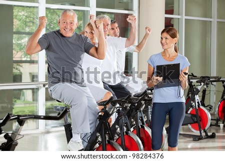 Cheering happy senior citizens with fitness trainer in gym