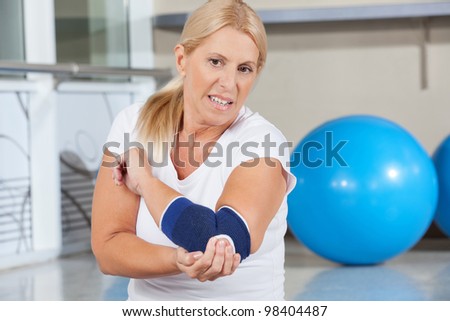 Elderly woman holding her aching elbow with bandage in gym