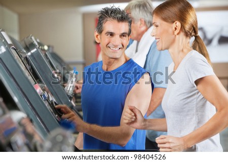 Fitness trainer explaining treadmill to jogging woman in gym