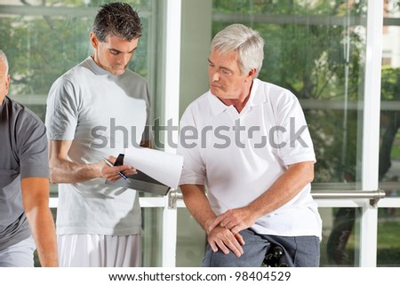 Fitness instructor explaining training plan for senior in gym
