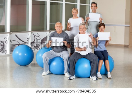Happy senior citizens on gym balls holding empty signs in fitness center