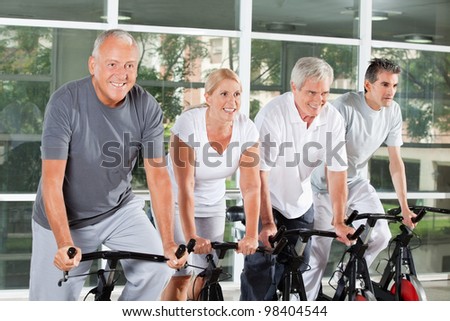 Happy senior people riding bikes together in fitness center