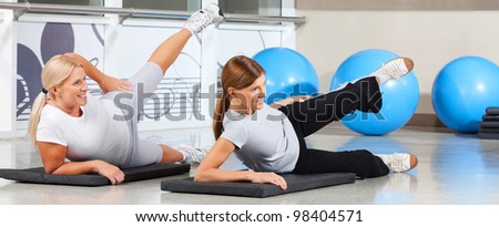 Two elderly women exercising together in fitness center on gym mats