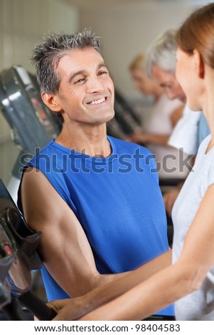 Fitness trainer flirting with woman on treadmill in gym
