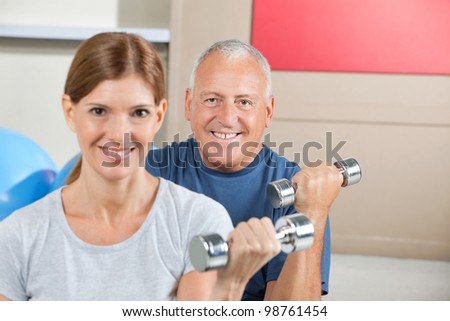 Two seniors lifting weights with dumbbells in fitness center