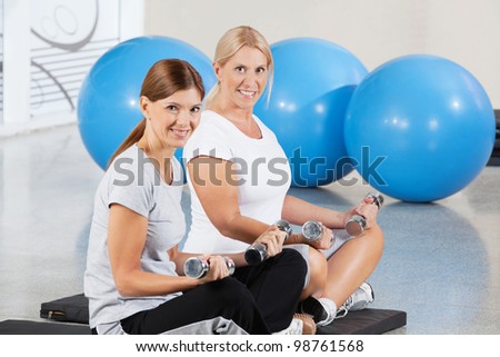 Two elderly women exercising with dumbbells on gym mats in fitness center