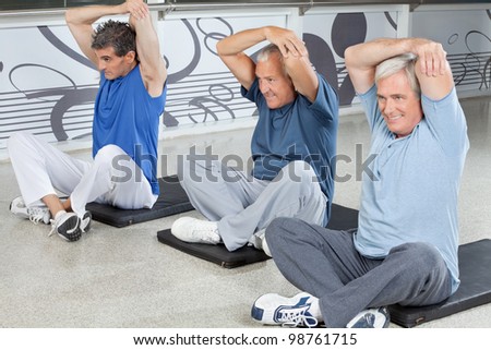 Elderly men stretching in fitness center on gym mats