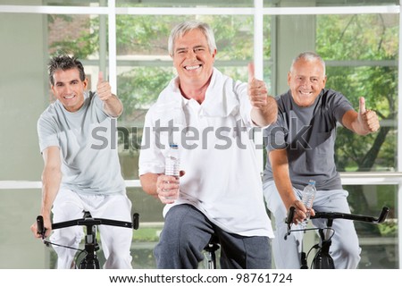 Three successful seniors holding thumbs up on bikes in gym