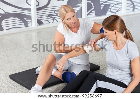 Woman with sports injury gets First Aid from fitness trainer in gym
