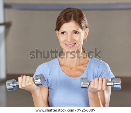Elderly smiling woman doing dumbbell training in gym