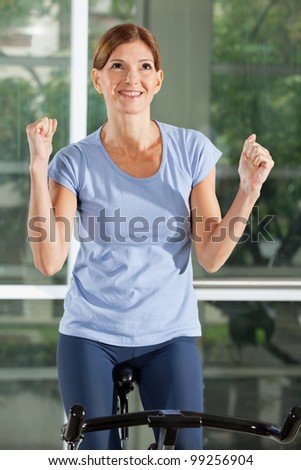 Cheering woman on bike in fitness center clenching her fists