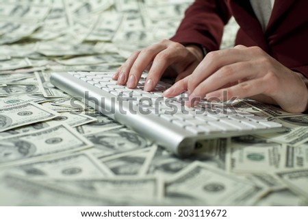 Womans typing at the desk covered with dollars bills