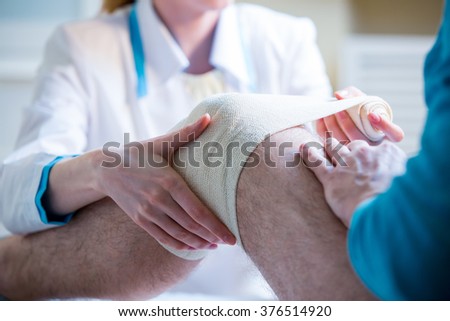 Female doctor is rewinding knee bandage to man. Doctor taking care of a patient with trauma of patella