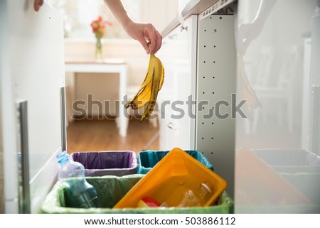 Woman putting banana peel in recycling bio bin in the kitchen. Person in the house kitchen separating waste. Different trash can with colorful garbage bags.