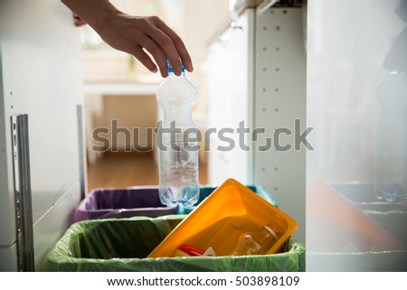 Man putting empty plastic bottle in recycling bin in the kitchen. Person in the house kitchen separating waste. Different trash can with colorful garbage bags.
