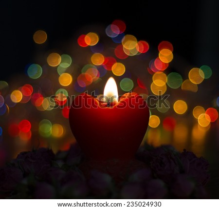 Red heart candle with roses on mistical colored lights and black background  and defocused effect