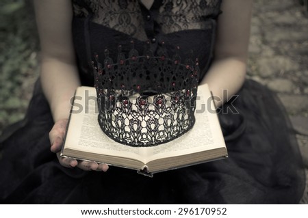 Woman in black dress holdings a book and crown