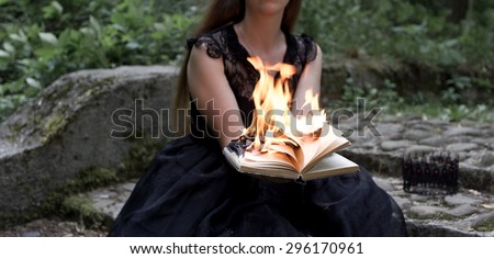A sitting woman in a black dress holds black burning book