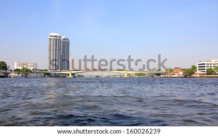 Chao Phraya river of Bangkok, Thailand. The photograph shows a bridge that crosses the river. The sky is spotlessly blue.