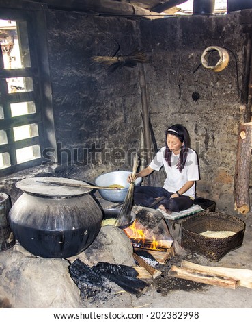 PUNAKHA, BHUTAN - MARCH 7, 2014: A bhutanese woman near Punakha is preparing food on a fire in her very simple kitchen.