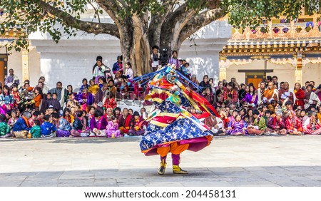 PUNAKHA, BHUTAN - MARCH 8, 2014: masked dancers at  drupchen festival in the dzong of Punakha, Bhutan. In the background are bhutanese spectators, watching the performance.