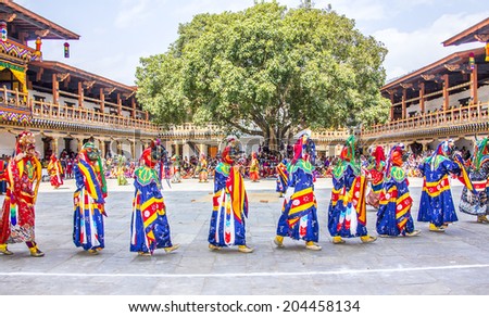 PUNAKHA, BHUTAN - MARCH 8, 2014: masked dancers at  drupchen festival walking in a row in the dzong of Punakha, Bhutan. In the background are bhutanese spectators, watching the performance.