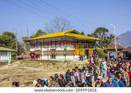 TASHIDING, INDIA - MARCH 16, 2014: At the bumchu festival, Tashiding, Sikkim, Buddhist believers, men and women,  are queuing in two lines to get into the temple. In the back is a beautiful temple.