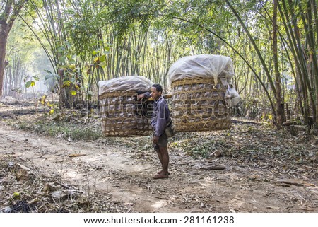 NIAUNGSHWE, MYANMAR - FEBRUARY 2, 2015: A man is carrying a big load in two baskets on his shoulder. He comes from a market at the bank of lake Inle, Myanmar.