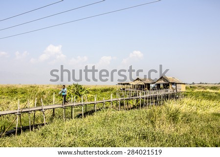 NIAUNGSHWE, MYANMAR - FEBRUARY 2, 2015: A stilt house at the bank of lake Inle, Myanmar. A man is walking along the stilted walkway.