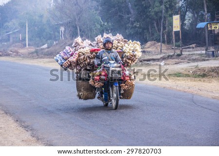 LOIKAW, MYANMAR - FEBRUARY 7, 2015: A street seller is driving his motorbike along a road near Loikaw, Myanmar. The bike is loaded with his merchandise.