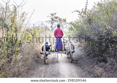 LOIKAW, MYANMAR - FEBRUARY 7, 2015: A farmer is driving his bullock cart along a rural dirt road near Loikaw, Myanmar.