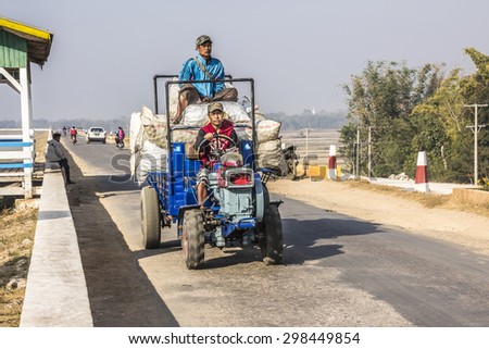 LOIKAW; MYANMAR - FEBRUARY 7, 2015: A tractor loaded with vegetables in white sacks is driving along a country road near loikaw, Myanmar. One person sits on top of the vegetables.