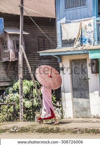 DAWEI, MYANMAR - FEBRUARY 15, 2015: A buddhist nun is walking along a street at Dawei, in the south of Myanmar. She is wearing a parasol.