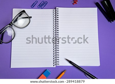 Empty notebook with office supply on purple background