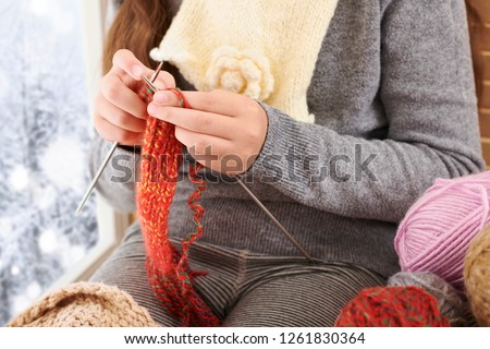 Child girl is sitting on a window sill with wool yarns and knitting. Beautiful view outside the window - sunny day in winter and snow.