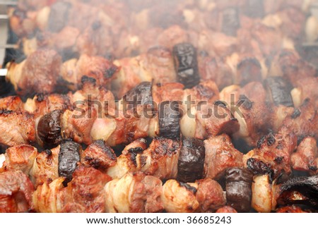 Preparation of meat slices with vegetables in sauce on fire. Smoke visible.