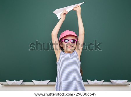 Schoolgirl with origami plane near school board