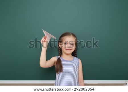 Schoolgirl with paper toy plane near school board