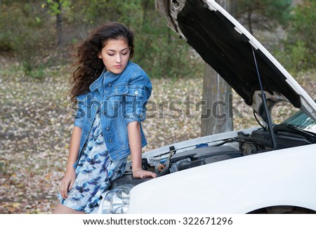 Woman with broken car inspecting engine