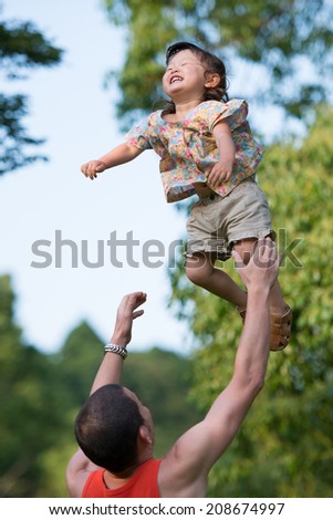 A happy two year old girl tossed into the blue sky by her father.