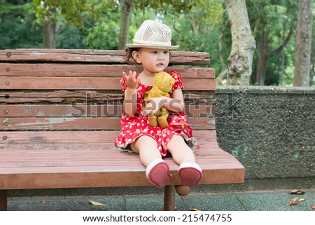 Cute Smiling Young Girl Hugging Her Teddy Bear on Bench Outside.