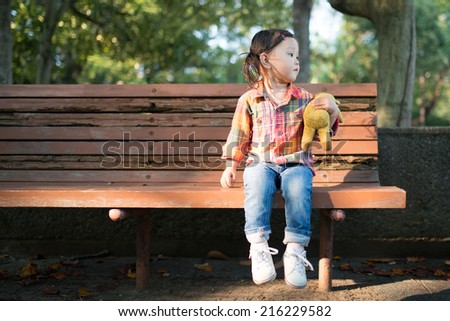 Cute Smiling Young Girl Hugging Her Teddy Bear on Bench Outside