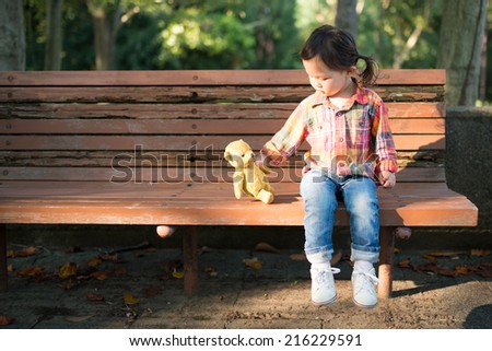 Cute Smiling Young Girl Hugging Her Teddy Bear on Bench Outside