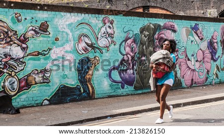 SHOREDITCH, LONDON, UK, June 8 2014: Street art in Shoreditch. Black woman walking holding her son, in front of  on a wall decorated in graffiti in Shoreditch.