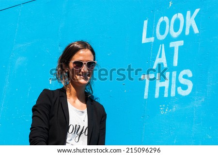 Hipster model wearing sunglasses posing next to a blue wall with the words \