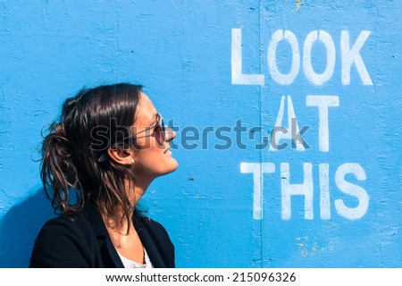 Portrait of a model wearing sunglasses posing next to a blue wall with the words \