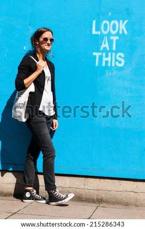 Hipster model wearing sunglasses posing next to a blue wall with the words 