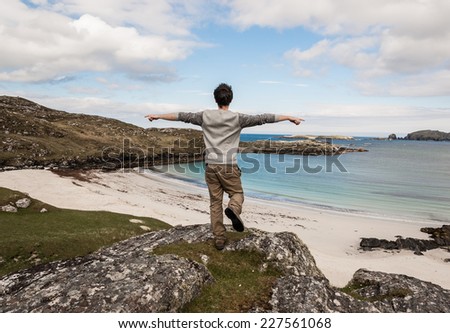 Young male tourist with open arms admiring a desert white beach with blue sea in the Isle of Lewis, Outer Hebrides, Scotland (UK).