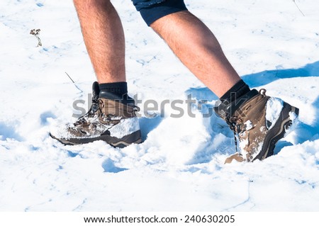Man walking in a path covered in snow. Focus on shoes and man legs